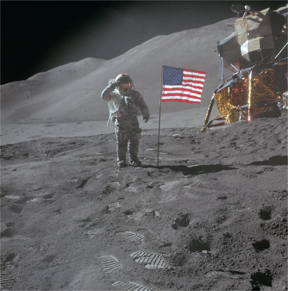 an astronaut in a white space suit spreads an American flag over a dusty blue moon