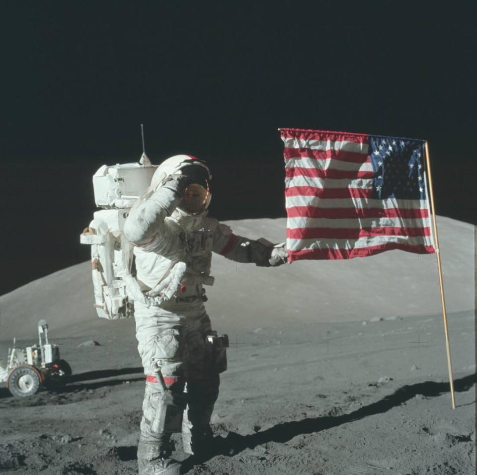 an astronaut in a white space suit spreads an American flag over a dusty blue moon