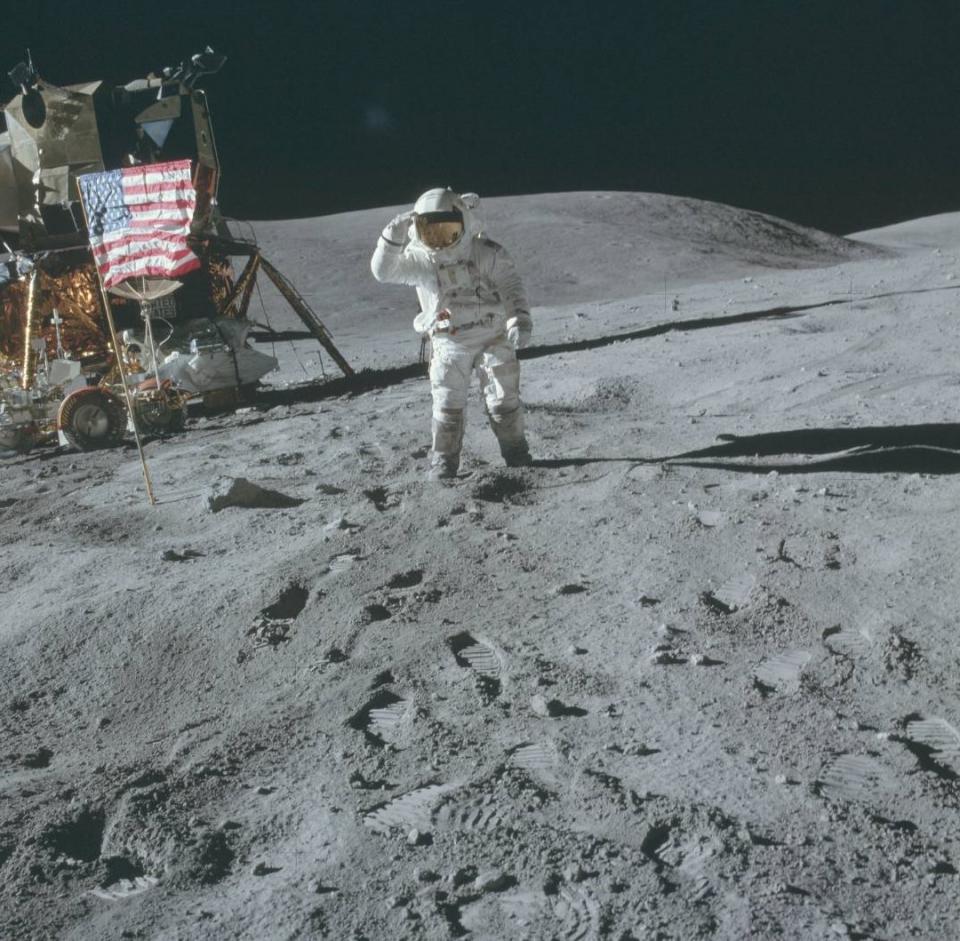 an astronaut in a white space suit spreads an American flag over a dusty blue moon